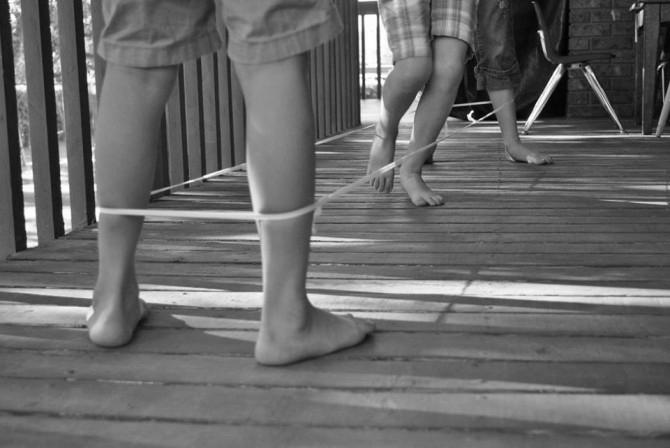 Δυο παιδιά κρατάνε το λάστιχο στα πόδια τους πρώτα με ανοιχτά πόδια στον αστράγαλο, στη συνέχεια στο γόνατο και τέλος στο μπούτι.