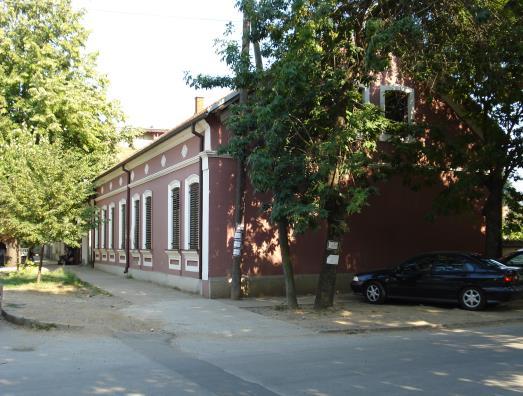 На заобљеном углу је улаз у апотеку, где су лево и десно аплицирана два емајлирана медањона са ликовима Хигије и Ескулапа. Бочна крила служе за становање.