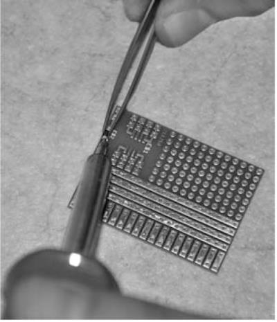 Fig. 46: În timp ce menţineţi în poziţie dioda SMD cu ajutorul pensetei, trebuie să încălziţi pad-ul cositorit şi conexiunea diodei. Fig.