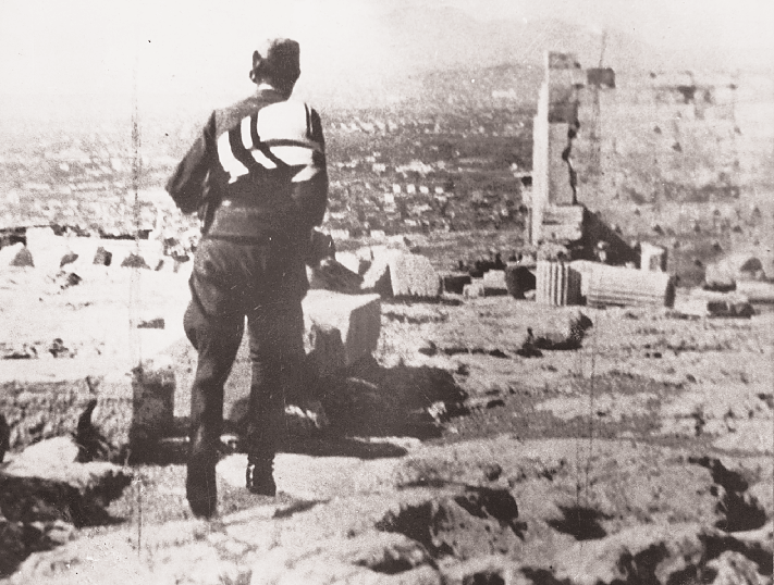 O τελευταίος Γερμανός στρατιώτης εγκαταλείπει την Aκρόπολη μεταφέροντας τη σημαία του. H σβάστικα δεν μολύνει πια τον Iερό Bράχο.