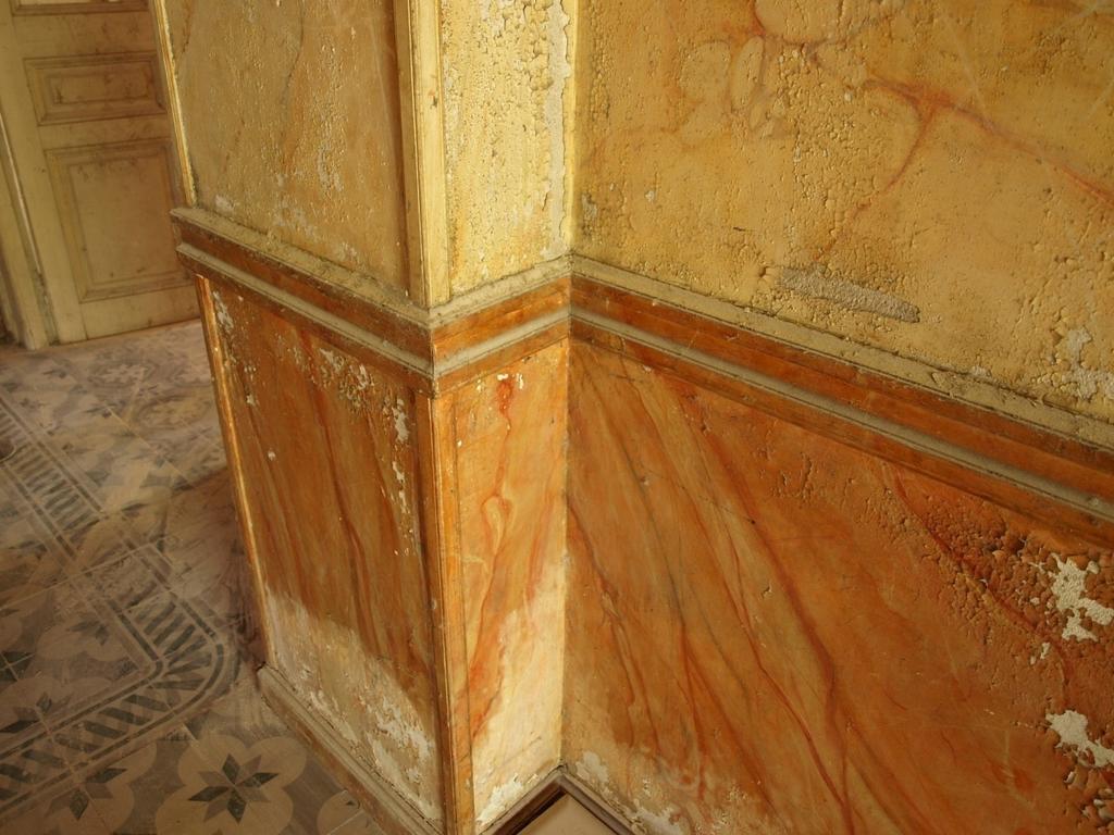 Σημαντική είναι και η φθορά που έχει υποστεί ο εντυπωσιακός ζωγραφικός διάκοσμος από απομίμηση μαρμάρου στην τοιχοποιία του ισογείου(εικ.26,27).