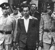1 του Γενάρη 1956 Ο Μιχάλης Καραολής οδηγείται στο δικαστήριο. Θα καταδικαστεί σε θάνατο και θα εκτελεστεί από τους Άγγλους με απαγχονισμό. Στις 12 τα μεσάνυχτα στις 31 του Δεκέμβρη σβήσαμε τα φώτα.