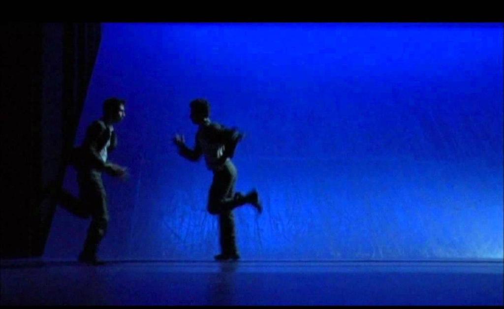ένας βγάζει ένα τσιγάρο και ζητά από τον άλλον φωτιά. Το σταθερό τρέξιμο παίρνει διαστάσεις αγώνα, καθώς οι διάδρομοι κινούνται με γρηγορότερο ρυθμό, ενώ αυτοί πασχίζουν για μια στιγμή επαφής.